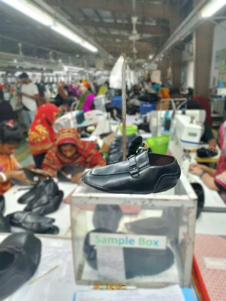 Black leather sample shoe displayed on a sample box in the production facility